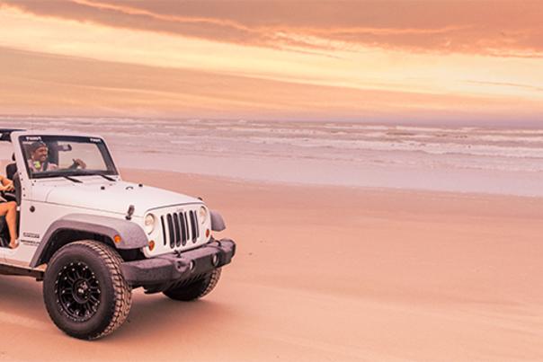 Two people in a jeep on the beach.