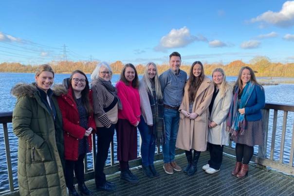 A group of people stood posing for a group photo on a balcony, with a lake behind them.