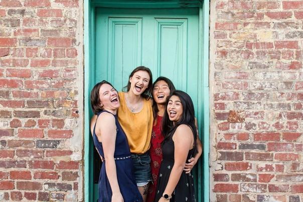 Four young women laughing in front of a light green door outside of the Grit.