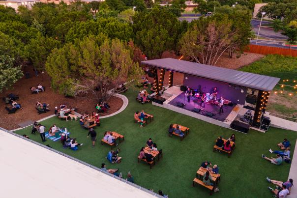 Aerial photo of the Meanwhile Brewing backyard with people sitting at picnic tables listening to live music.