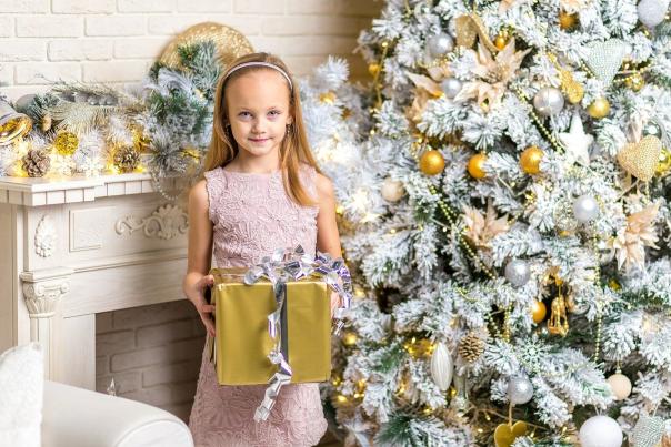 Young girl holding a present in front of a tree