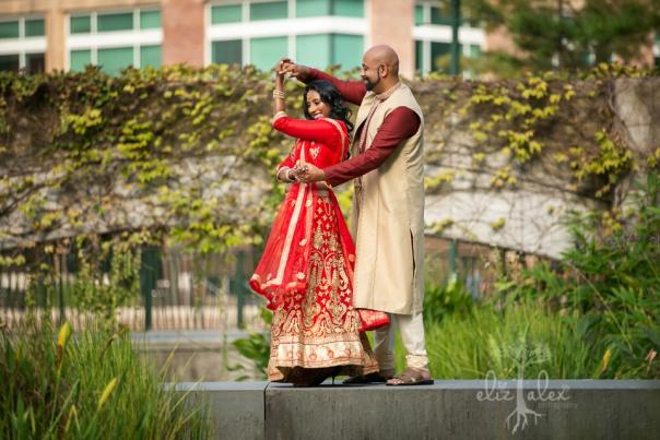 An Indian couple dances on an island at the Koi Garden on The Woodlands Waterway. The woman is wearing a long red-and-white dress with gold bracelets. The man is wearing a maroon shirt and long tan overcoat.