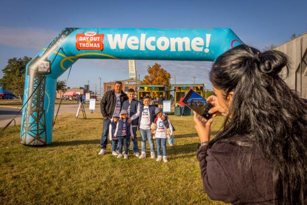 Woman taking picture of family under Day Out with Thomas welcome sign
