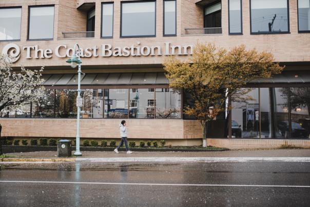 A person walking in the rain in front of the coast bastion inn.