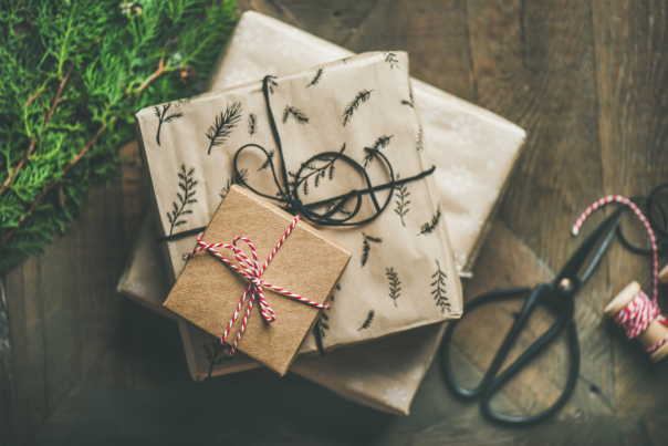 Stack of Christmas presents wrapped up with garland and scissors in the back on a wood background