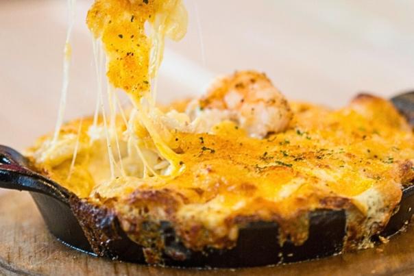 Seafood dip with a cheddar cheese pull of creamy seafood from a black cast iron pan.