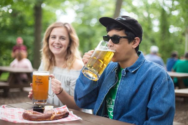 Two people at Hubbard Park Beer Garden, drinking beer over a large hot pretzel.