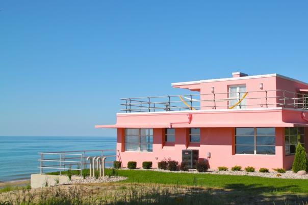 Beautiful pink house atop a dune in front of a lake.