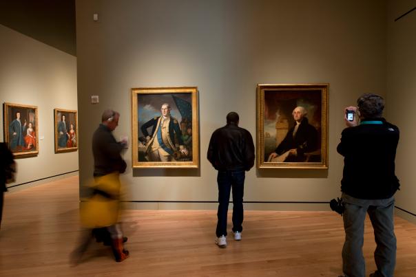 Visitors explore an art gallery featuring portraits of President George Washington in ornate frames.