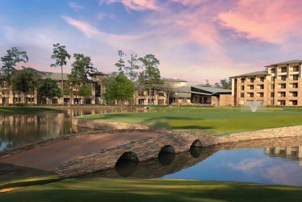 A sunset view of The Woodlands Resort and Back Table Kitchen from the golf course. Between the viewer and the hotel is a short brick footbridge across a pond with a small fountain.