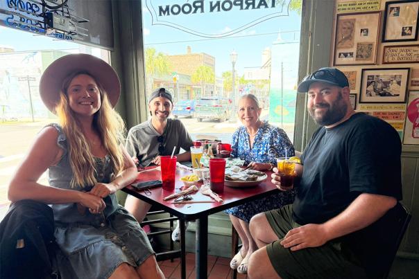 Two men and two women sit at a restaurant table in the corner beside windows looking out on to the street