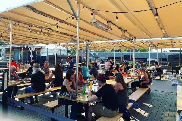 People sit at picnic tables under a large tent enjoying beers