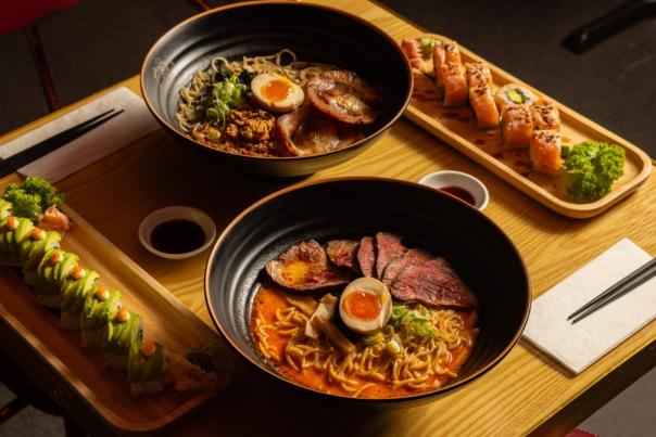 Big bowls of ramen dishes with egg, noodles and beef along side sides of sushi at Maki & Ramen