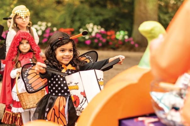 Girl dressed as monarch butterfly for Halloween holding out candy bag at SeaWorld San Antonio