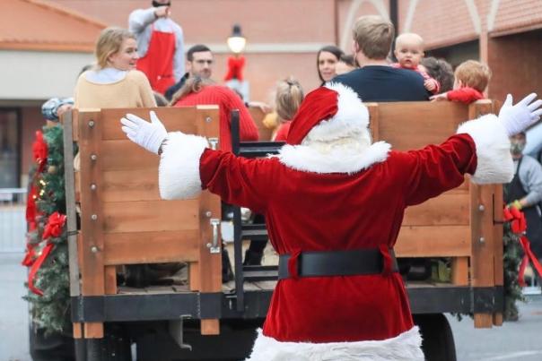 Santa is shown from the back. In front of him you can see several people on a holiday hay ride.