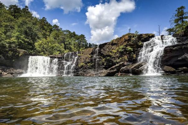 Beautiful cascading waterfall against blue sky with puffy white clouds.