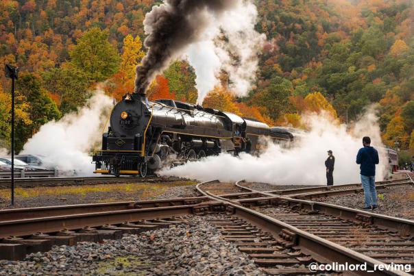 A steam train puffs along the tracks in Jim Thorpe, PA against a backdrop of colorful fall foliage.