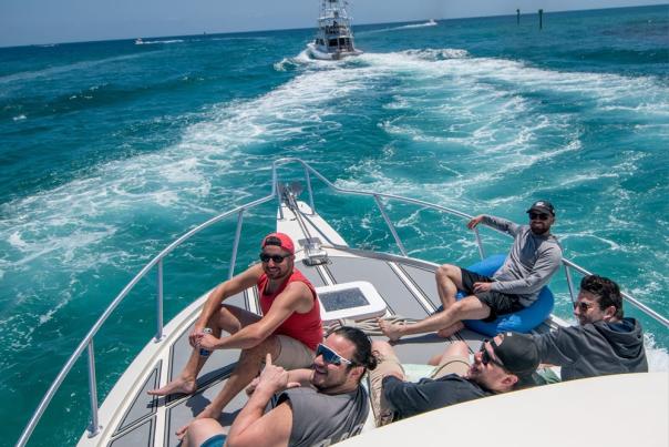 Five guys sitting on the bow of a fishing boat heading out to go fishing in beautifully clear blue waters off Pompano Beach.