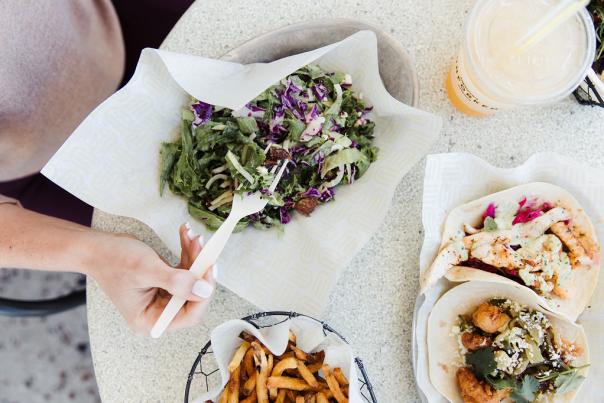 Person using fork to eat a salad, tacos and fries at Unforked