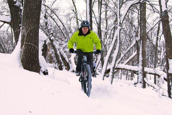 guy in green coat biking in the snow