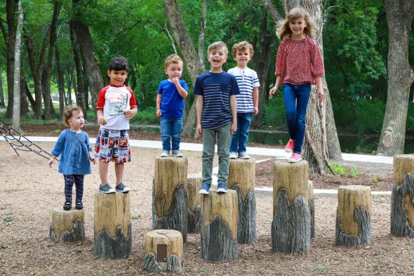 kids standing on tree stumps at varying heights in a park