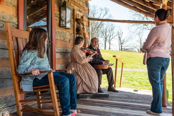 a young girl and woman enjoy music being played on the porch of a log cabin