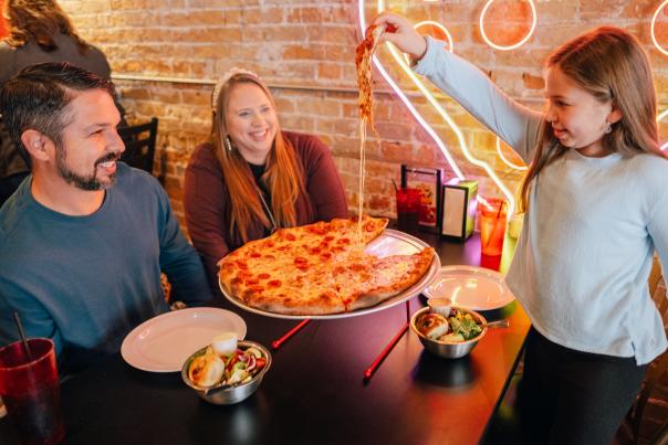 A family enjoys a very cheesy pizza at Valentino's in Downtown San Marcos