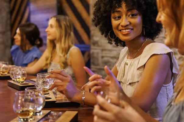 Women at a bar tasting bourbon and talking.