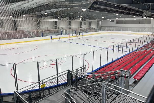 An image of an empty ice rink at the Rochester Ice Center complete with red bleacher seats.