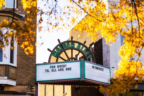 An old-fashioned marquee for Maiden Alley Cinema stands at the opening of an alley in downtown Paducah. The yellow fall leaves frame the picture and one side of the marquee reads "Oktoberfest."