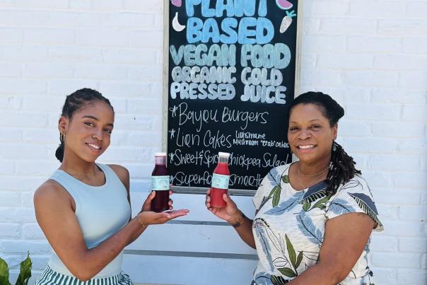 Alicia and Carmen Norman of The Earthly Elephant display their bottled juices, seated outdoors on a bench.