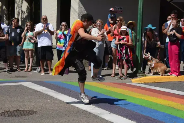 A person with a rainbow cape dancing on a pride crosswalk.