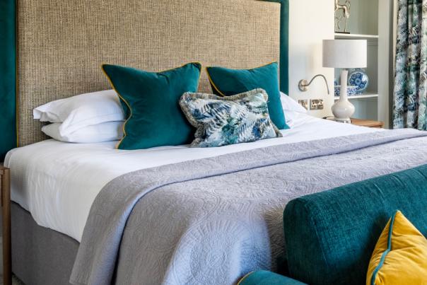 A double bed with teal cushions and a grey cover, with a teal sofa in front of it