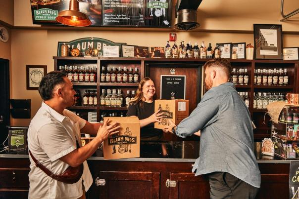 Two people in front of a counter, holding boxes that they purchased from someone standing behind the bar.
