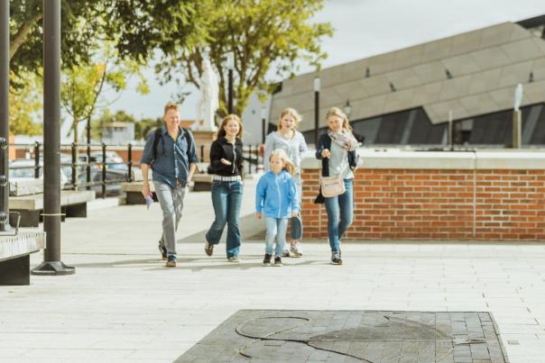 Family walking along Hull’s waterfront near The Deep, passing a large stingray sculpture embedded in the pavement on the Hull Fish Trail, with modern architecture and open public space creating a lively sightseeing atmosphere