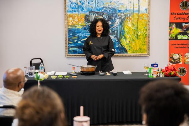 a group sits and listens as a woman leads a gumbo cooking class