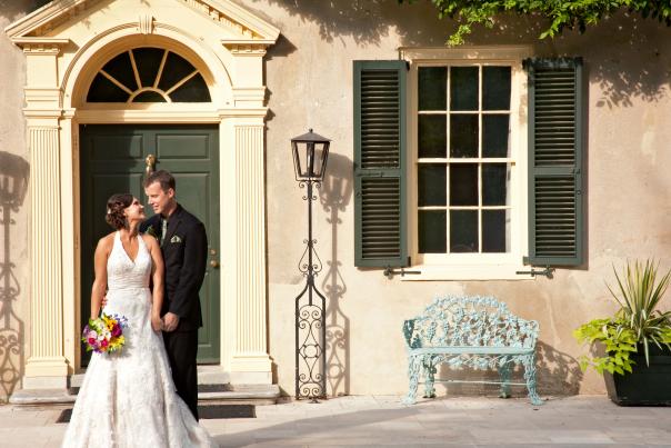 Woman in wedding dress holding bouquet next to man in a suit in front of the entrance to Hagley