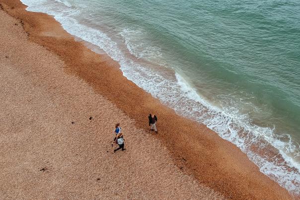 Aerial photograph showing three people walking along the beach near the sea edge