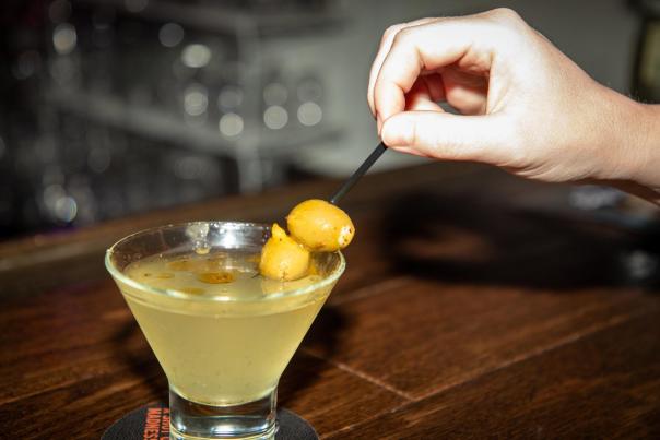 Person mixing a cocktail with a pick that has olives on it.