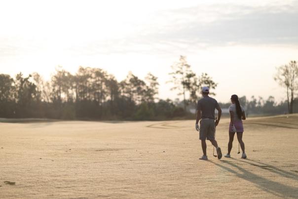 man and woman walk on golf course with golf clubs