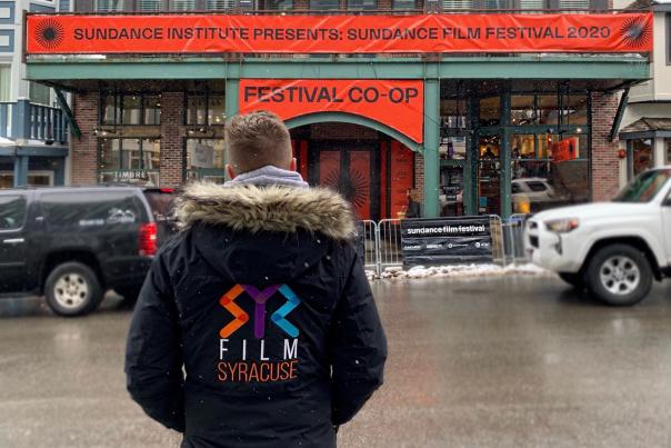 a man standing with a syr film office logo looking at a sundance film festival theater