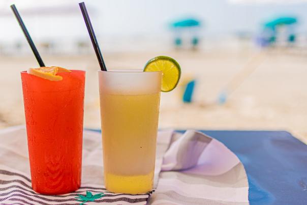 Two cocktails sitting on the beach, one is red one is yellow. Thye are sitting on a towel.