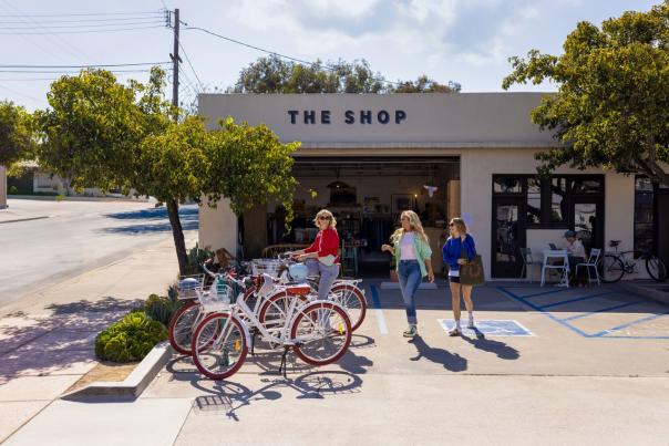 Three women walking to bikes parked outside of a building called "The Shop"