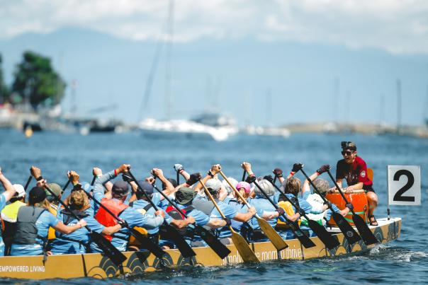 A large group of people canoeing in one canoe with a pacer sitting at the front of the caneo.