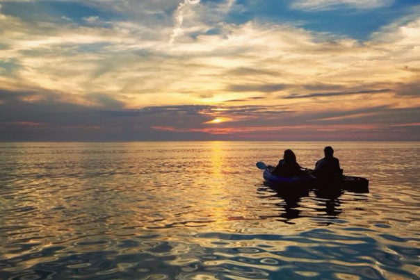 a couple in kayaks are silhouetted against the sunset over Lake Michigan