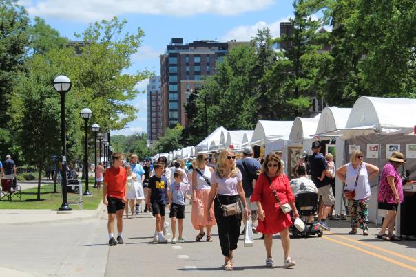 People walking around browsing art vendors stationed in white tents lining the pedestrian only street