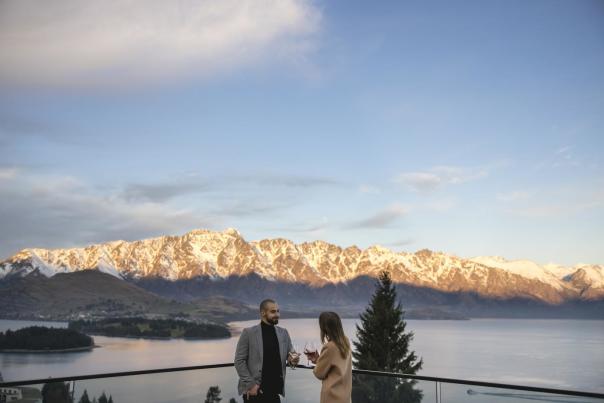 People enoying a wine on the balcony of Nest Kitchen and Bar overlooking the snow-covered Remarkables mountain range
