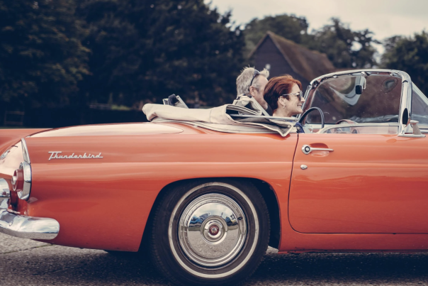 empty nest blog cover. older couple riding in a red Thunderbird convertible.