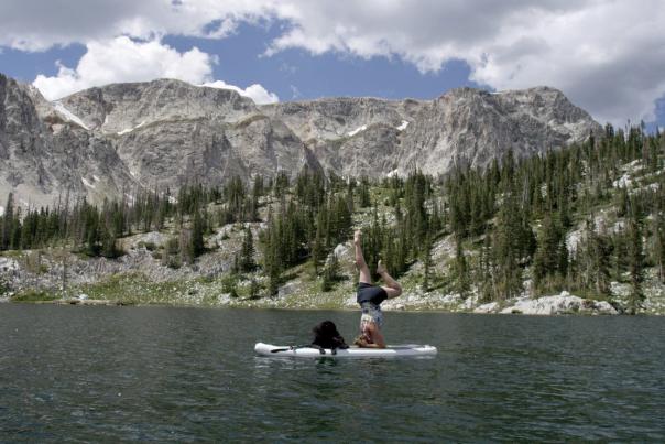 Person doing yoga on a paddleboard with their dog.