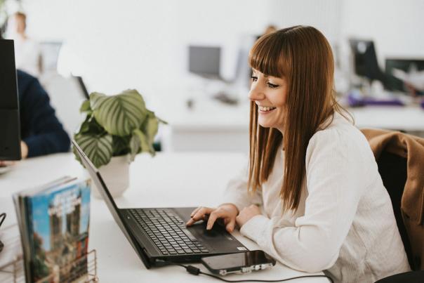 a woman smiling and working at a laptop in an office with plants